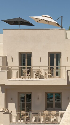 A two-story building with a balcony, outdoor furniture, and umbrellas. - Infinity Suites 1, By Hellocrete (Rethymno)