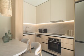 Een moderne keuken met een ronde eettafel, twee stoelen, een inbouwoven, een vaatwasser, een magnetron en een spoelbak.