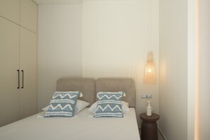 Een slaapkamer met een bed, twee kussens, een nachtkastje, een lamp en een kledingkast.
