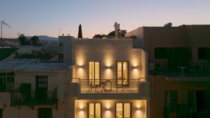 A multi-story building with balconies, a statue on the roof, and a cityscape in the background. - Infinity Suites 2, By Hellocrete (Rethymno)