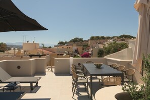 Une terrasse extérieure avec une table et des chaises, donnant sur un quartier résidentiel avec des immeubles et des montagnes en arrière-plan.