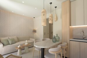 Ein modernes Wohnzimmer mit Sofa, Esstisch und Stühlen, einem Küchenbereich mit Spüle und Pendelleuchten.