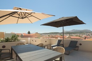 Une terrasse sur le toit, avec une table, des chaises et deux parasols.