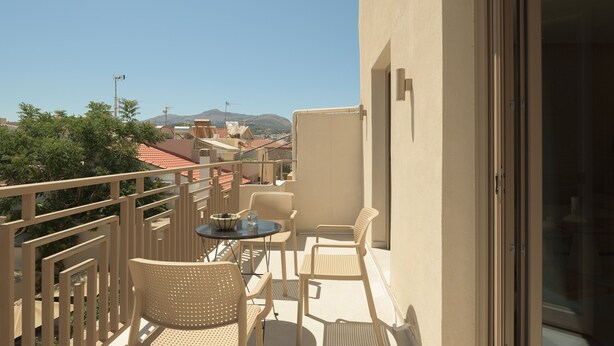 A balcony with a table and chairs, a view of buildings and hills in the background. - Infinity Suites 2, By Hellocrete (Rethymno)