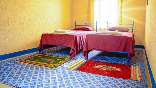 Een kamer met twee bedden, een raam met gordijnen en vloerkleden met een patroon.