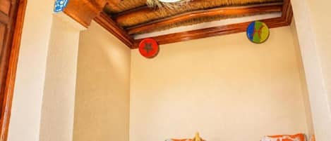 A room with a wooden ceiling, a hanging light fixture, a wall clock, and a small table with a basket.