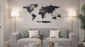 A living room with a grey sofa, two lamps, a world map on the wall, and a glass coffee table with a vase. - Comfortable English Appartment Walk to A Union Market (Washington)