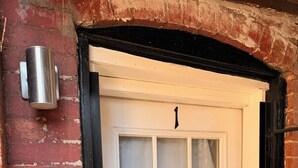 A white door with a frosted glass window, a metal doorbell, and a brick wall with a number '1' above the door. - Comfortable English Appartment Walk to A Union Market (Washington)