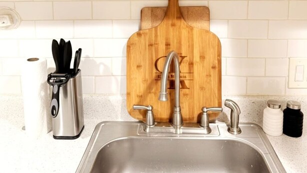 A kitchen with a stainless steel sink, a wooden cutting board, and a cabinet with glassware. - Comfortable English Appartment Walk to A Union Market (Washington)