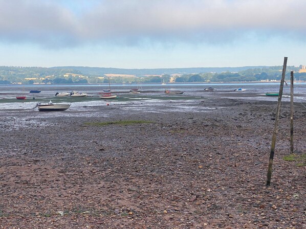 A rocky beach with boats and a distant view of hills.