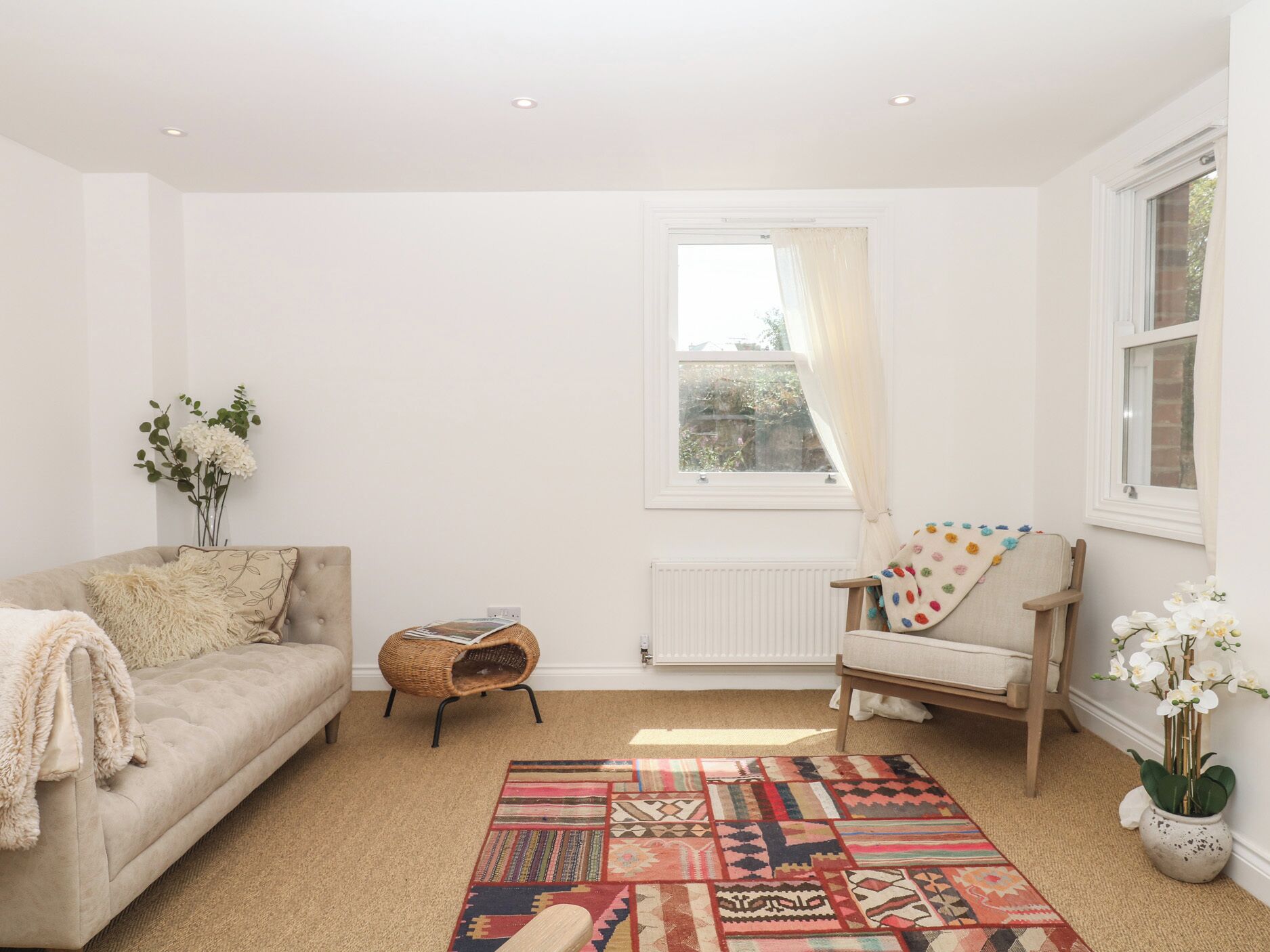 Un salon comprenant un canapé, un fauteuil, un tapis à motifs, un radiateur et une fenêtre avec des rideaux.