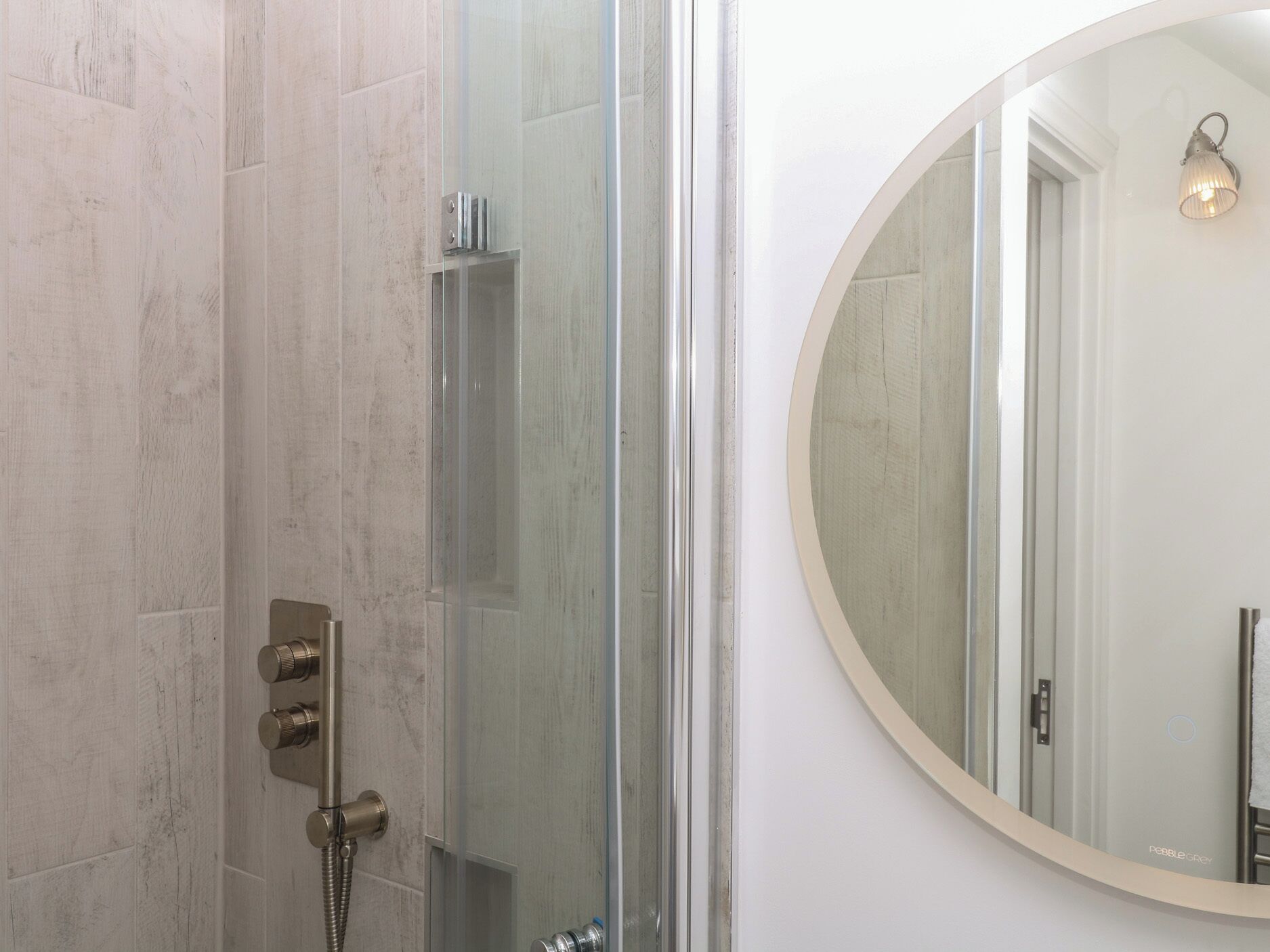 Baño con cabina de ducha de vidrio, espejo redondo e iluminación empotrada en la pared.