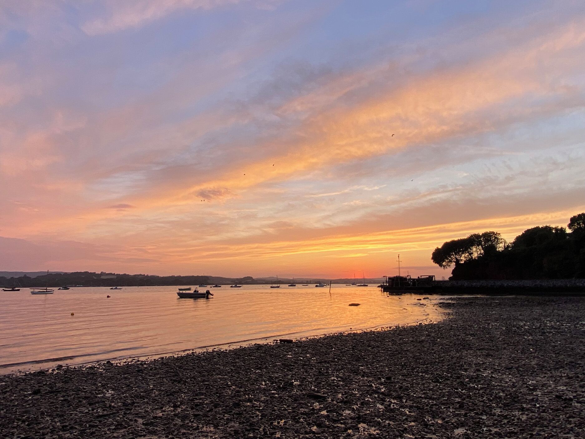 Eine Küstenlandschaft mit Booten auf ruhigem Wasser, einer felsigen Küstenlinie und einem Abendhimmel.