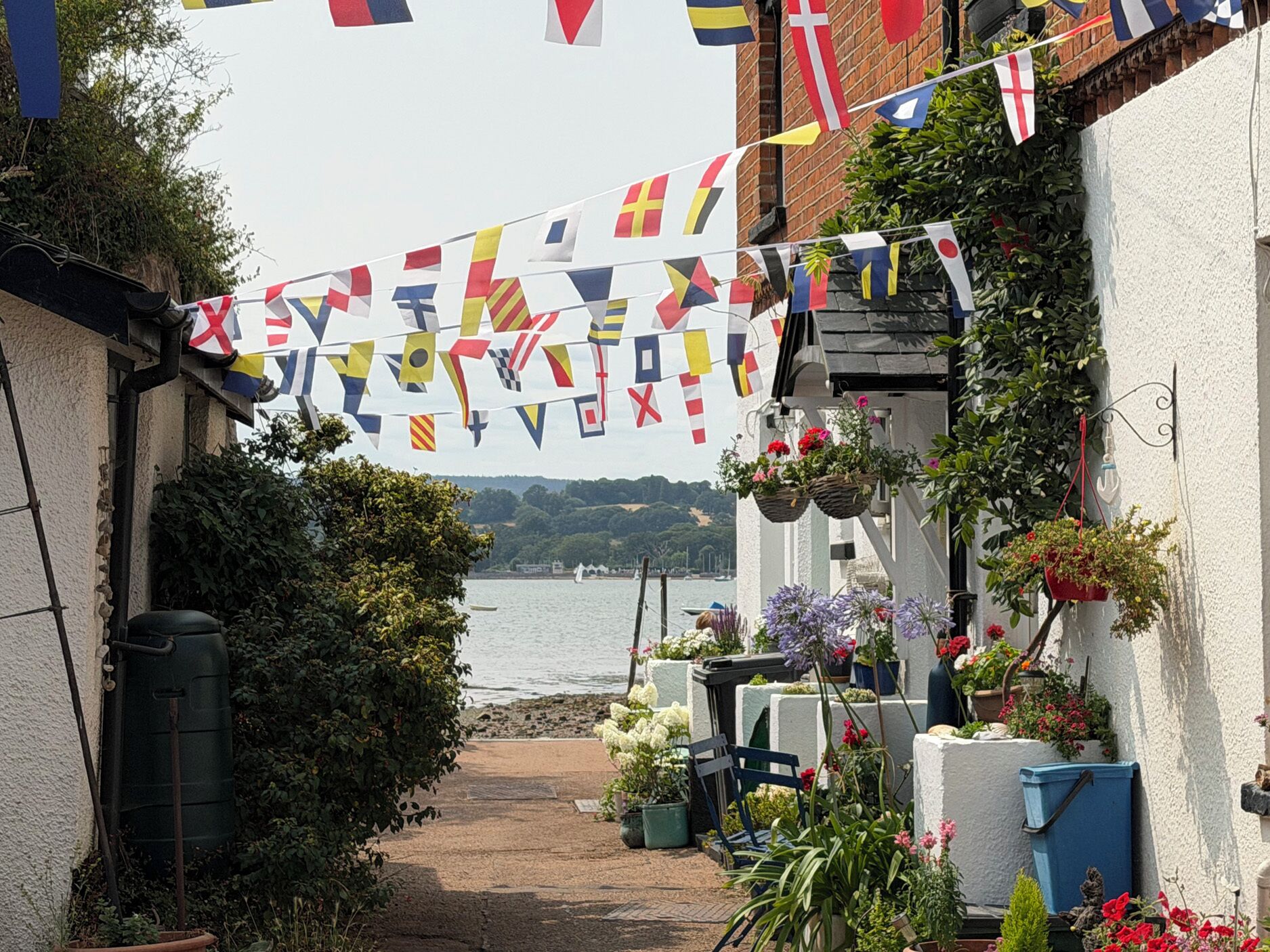 A narrow pathway leading to a building with a view of the sea. Flags are strung across the pathway.