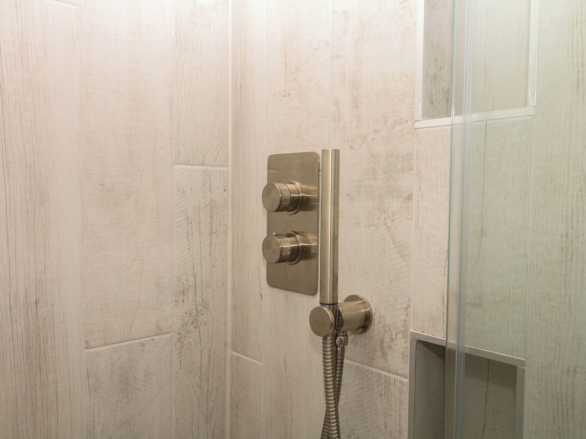 Ducha con cabezal de ducha de mano y panel de control en la pared.