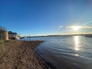 A pebbled beach with a clear sky and the sun reflecting on the water. - Alongside (Exmouth)