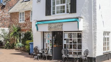 Un edificio blanco con contraventanas negras, un letrero que dice 'Susannah's Tea Room' y mesas al aire libre con sillas de metal.