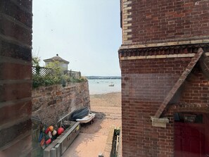 Vista de uma praia, com um prédio de tijolos e uma construção pequena ao fundo.
