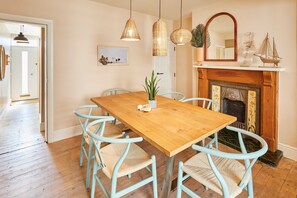 A dining room with a wooden table, light blue chairs, hanging wicker lamps, a fireplace, and a mirror above it. - Host Stay Casa Formentera (Scarborough)