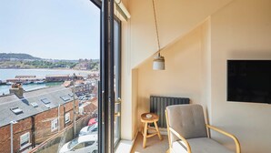 Een balkon met uitzicht op een kustplaats, een stoel, een klein krukje en een hangende lamp.