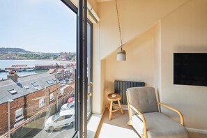 A balcony with a view of a coastal town, a chair, a small stool, and a hanging light fixture. - Host Stay Casa Formentera (Scarborough)