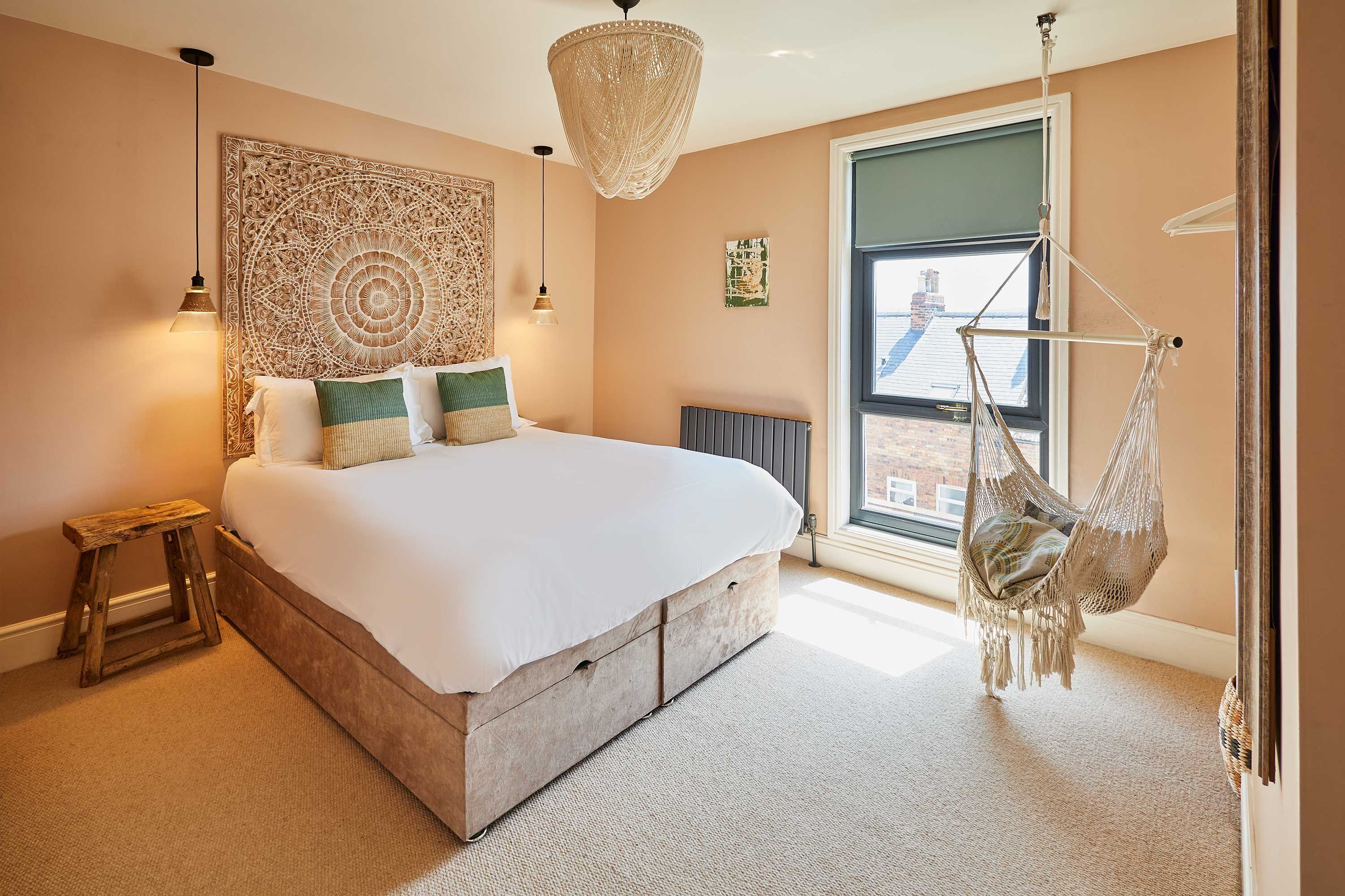 Ein Schlafzimmer mit einem großen Bett, einem Hängekorbstuhl, einer Wandteppich und Blick auf die Stadt durch ein Fenster.