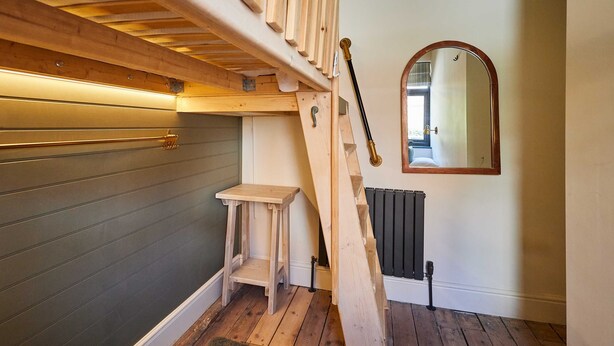 Een houten trap met een kleine houten bank aan de onderkant, een radiator en een spiegel aan de muur.