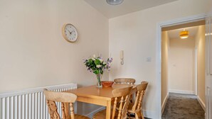 A dining area with a wooden table and chairs, a clock on the wall, and a flower vase. - Host Stay - Abbey House Sea View (Worthing)