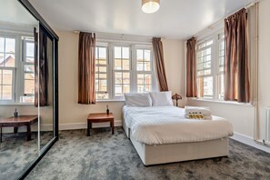 Ein Hotelzimmer mit einem großen Bett, einem kleinen Tisch, einem Spiegel und einem Fenster mit Vorhängen.