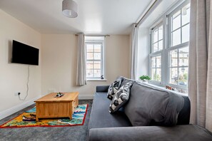 Ein stilvolles Wohnzimmer mit einer Couch, einem Couchtisch, einem Fernseher und großen Fenstern.