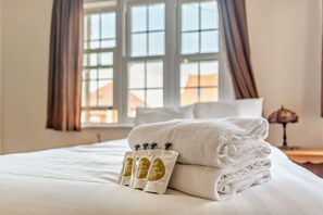 Cama arrumada com uma toalha branca dobrada e um conjunto de produtos de higiene.