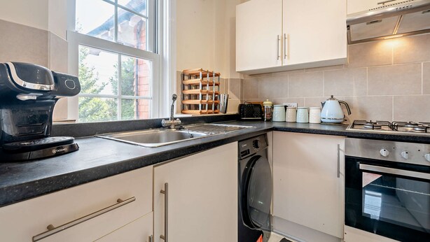 A modern kitchen with a built-in dishwasher, a coffee maker, and a stove. - Host Stay - Abbey House Sea View (Worthing)