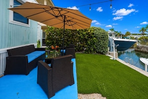 A patio with outdoor furniture, a table with flowers, a swimming pool, and a boat docked by the water. - Modern Summer Vibes • 40' Dock • Oceanside (Key Largo)