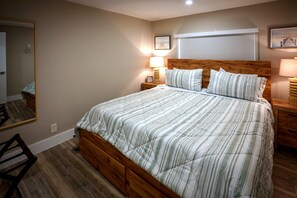 Quarto com estrutura de cama de madeira, um espelho grande, duas mesas de cabeceira com luminárias e cabeceira fixada na parede.