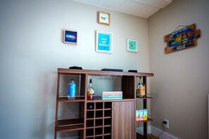 A room with a wooden cabinet containing various items, a wall with framed motivational posters, and a shelf with bottles and a box labeled 'HAPPY HOUR'. - Modern Summer Vibes • 40' Dock • Oceanside (Key Largo)