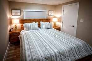 Ein ordentlich bezogenes Bett mit Streifenmuster, zwei Nachttischlampen und gerahmte Bilder an der Wand.