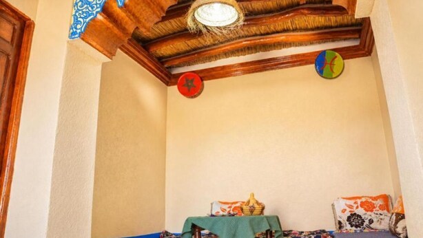 Een kamer met een houten plafond, een hanglamp, een wandklok en een tafeltje met een mandje.