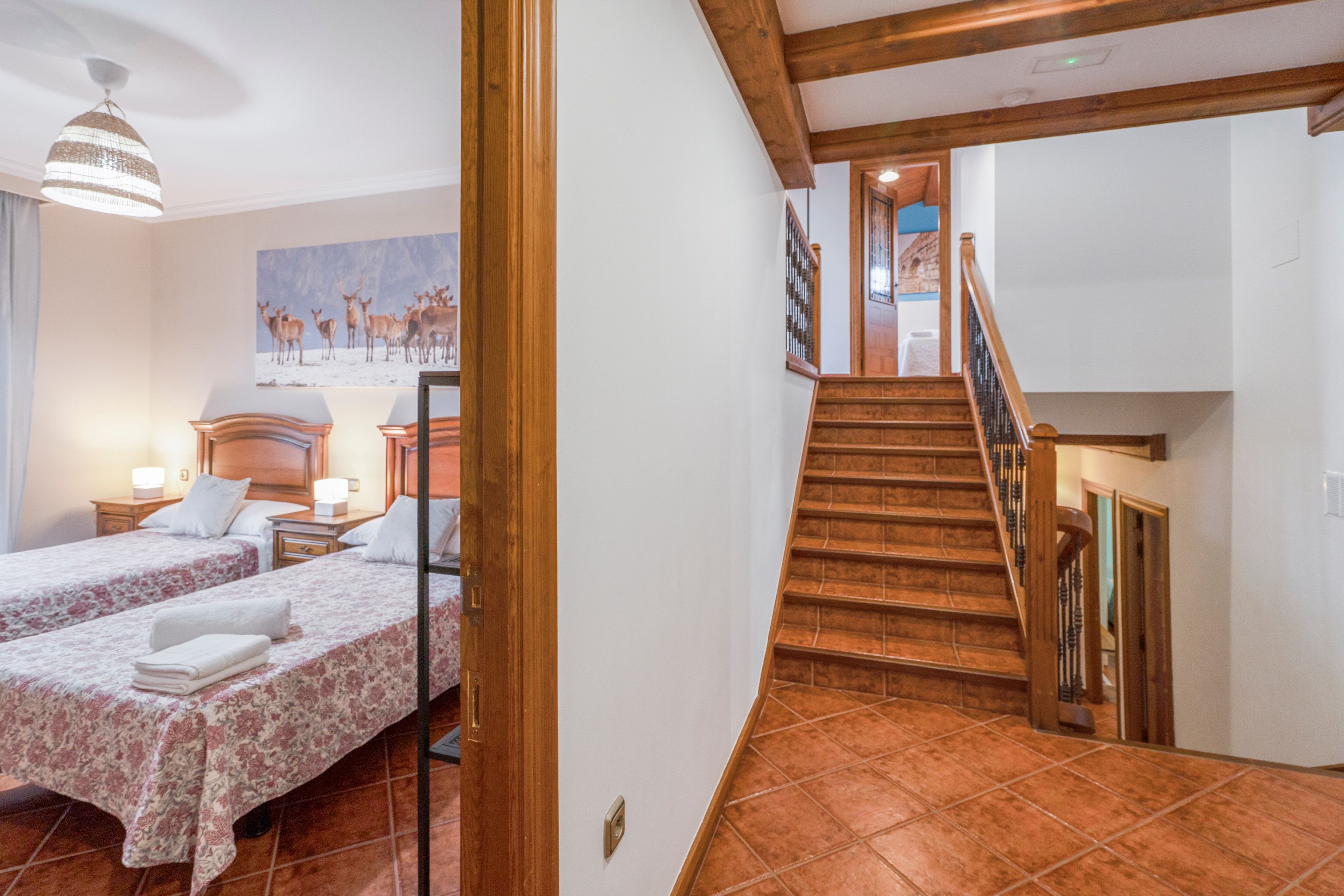 A hotel room with two beds, a staircase, and a painting of deer on the wall.