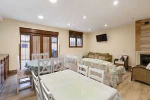A bedroom with two beds, a television, a fireplace, and a dining area with a table and chairs. - La Casona De Cuéllar: Rural House for Groups with Pool in Segovia (Cuéllar)