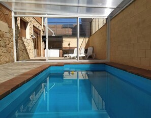 A swimming pool with clear blue water, surrounded by a stone wall and a glass enclosure. - La Casona De Cuéllar: Rural House for Groups with Pool in Segovia (Cuéllar)