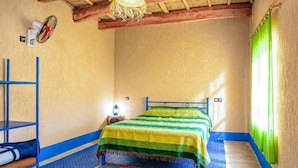 Een kamer met een bed, een blauwe plank, een kamerbreed tapijt met een patroon, en een raam met groene gordijnen.