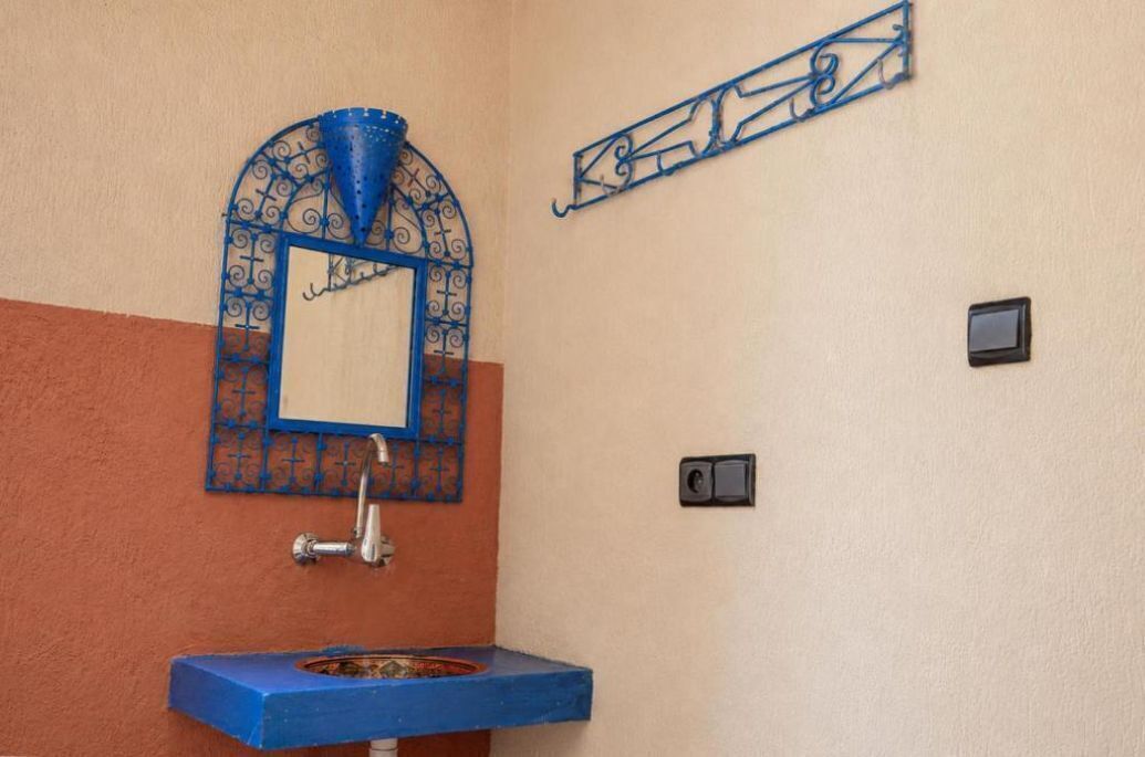A bathroom with a blue sink, a decorative mirror, and a wall-mounted light fixture.