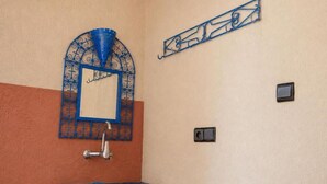 Een badkamer met een blauwe wastafel, een decoratieve spiegel en een wandlamp.