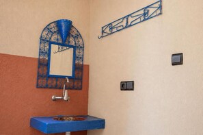 Une salle de bain avec un lavabo bleu, un miroir décoratif et un luminaire fixé au mur.