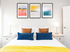 Una habitación de hotel con una cama, dos mesitas de noche, un armario blanco y tres cuadros en la pared.