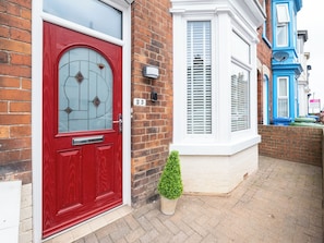 A red door with a glass panel, a white window with shutters, and a small potted plant on the ground. - 23 Trafalgar Road (Scarborough)