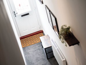 Een hal met een witte deur, een deurmat, een radiator en een tafeltje met een plant.