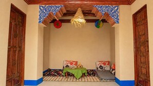 Une pièce au décor traditionnel, avec un plafond en bois, un luminaire suspendu en fibres tressées et un banc recouvert d’un tissu vert.