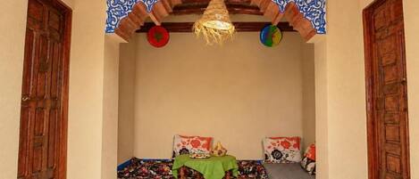 A room with a traditional design, featuring a wooden ceiling, a woven hanging light fixture, and a small table with a green cloth.