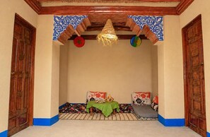 A room with a traditional design, featuring a wooden ceiling, a woven hanging light fixture, and a small table with a green cloth.